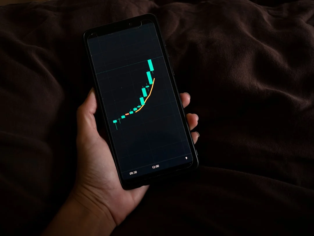 Des mains utilisant une application de trading sur smartphone avec des graphiques, des billets de dollar en arrière-plan.